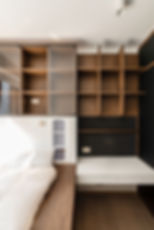Modern bedroom with wood shelves, white bedding, and a white desk. Bright sunlight illuminates the space, creating a calm atmosphere.
