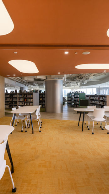 Secondary Library, VSA, Commercial Interior Design
Modern library interior designed by MAD Studio, featuring sleek white tables and chairs, vibrant orange ceiling, and built-in bookshelves. The contemporary open space offers a calming atmosphere with natural light and an inviting layout.