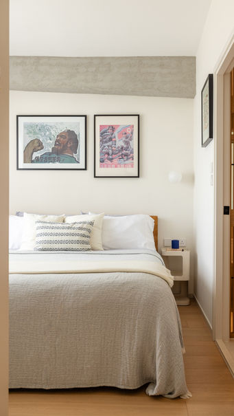 Modern bedroom interior design by MAD Studio featuring a cozy bed with white and patterned pillows, soft gray bedding, and minimalist wooden side table. Wall art with bold, colorful prints above the bed adds an artistic touch, while the neutral color palette and clean lines create a serene and stylish atmosphere. Ideal for showcasing contemporary home aesthetics and bedroom inspiration.