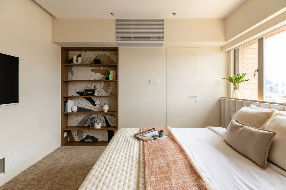 Modern bedroom interior design featuring neutral tones and minimalist decor. The room includes a stylish built-in wooden bookshelf with artistic wallpaper accent, a comfortable bed with plush pillows and a cozy orange throw. Large windows bring in natural light, highlighting the elegant and serene atmosphere. Ideal for showcasing contemporary home styling and interior design inspiration.