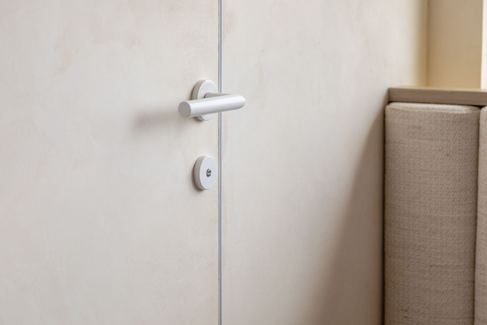 Close-up of a modern interior door design featuring a sleek metal handle and a textured beige wall. The minimalist style and neutral tones create a sophisticated and elegant look, ideal for contemporary home decor. Perfect for interior design inspiration and home renovation ideas.