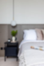 Minimalist bedroom with a wooden headboard, gray bedspread, pendant light, black nightstand, plant, and candles. Calm and cozy ambiance.