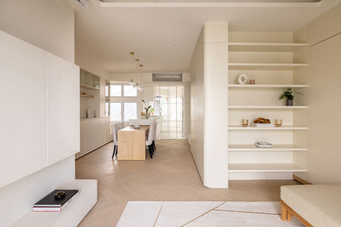 Modern living room, warm white colour tone, beige sofa, orange cushions, white area rugs with geometric pattern, TV cabinet and TV wall in microcement finish, decorative light trough, wooden perforated panels