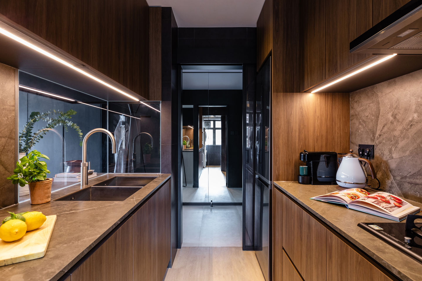 Modern kitchen interior design featuring sleek wood cabinetry, stylish LED lighting, and contemporary stone countertops. The compact space includes a polished chrome faucet, built-in appliances, and strategically placed decor elements like a potted plant and fresh lemons. Ideal for small spaces, this kitchen showcases minimalist elegance and efficient use of space. 