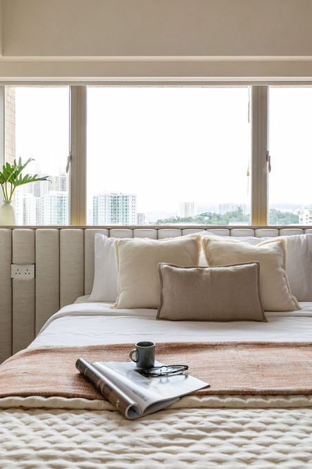 Cozy modern bedroom interior with neutral-toned pillows and a textured throw on a stylish bed. A magazine, pair of glasses, and a coffee mug add a touch of relaxation and comfort. Perfect for an inviting and serene design.