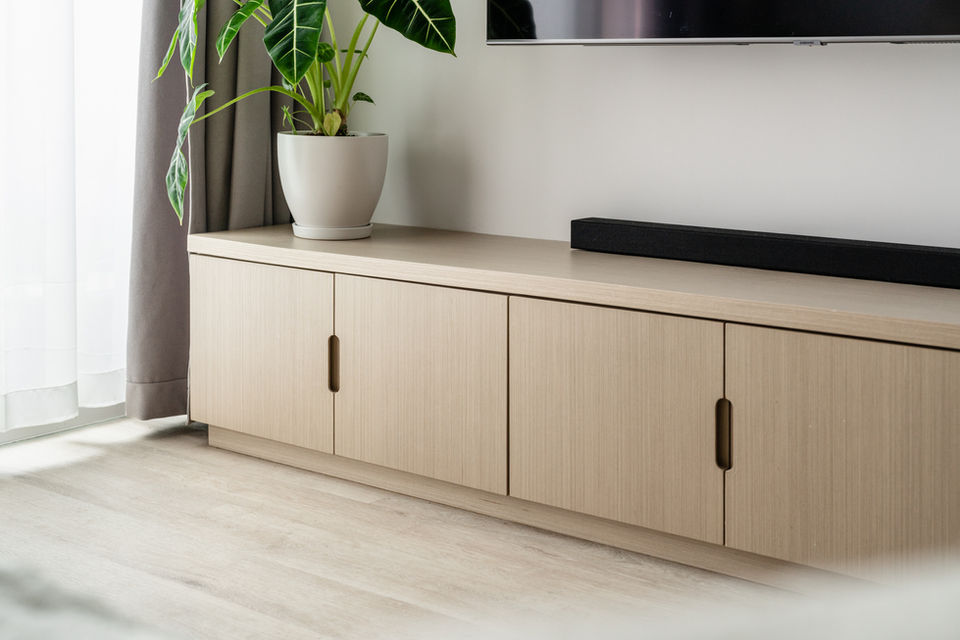 Modern living room interior design showcasing a minimalist light wood cabinet with sleek handles, complemented by a potted green plant and stylish black soundbar. Sunlight filters softly through sheer curtains, highlighting the room's contemporary elegance. Ideal for adding a touch of nature to modern home decor.